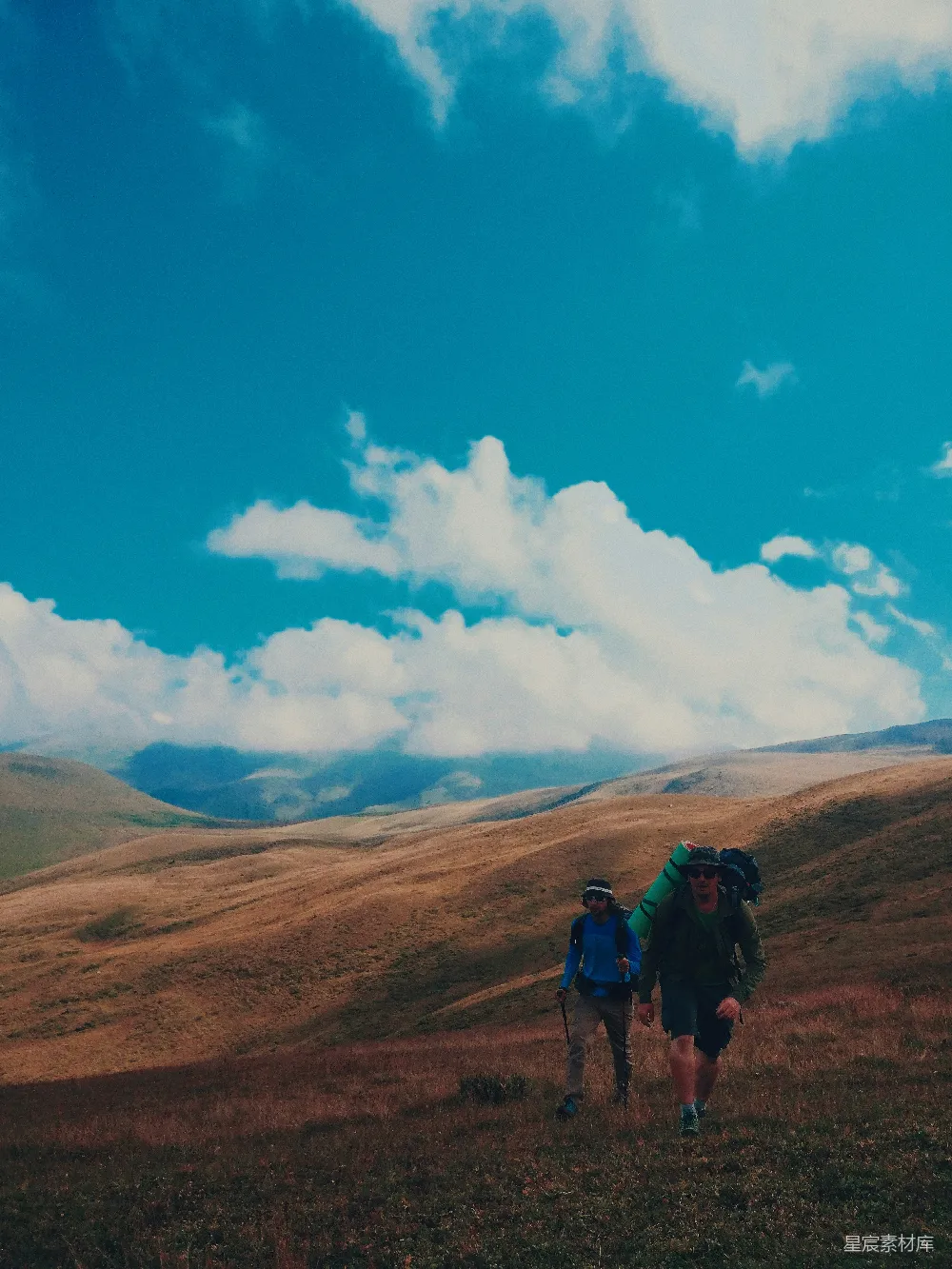 高清摄影  人们在白天的蓝天白云下，褐色的山上徒步旅行。