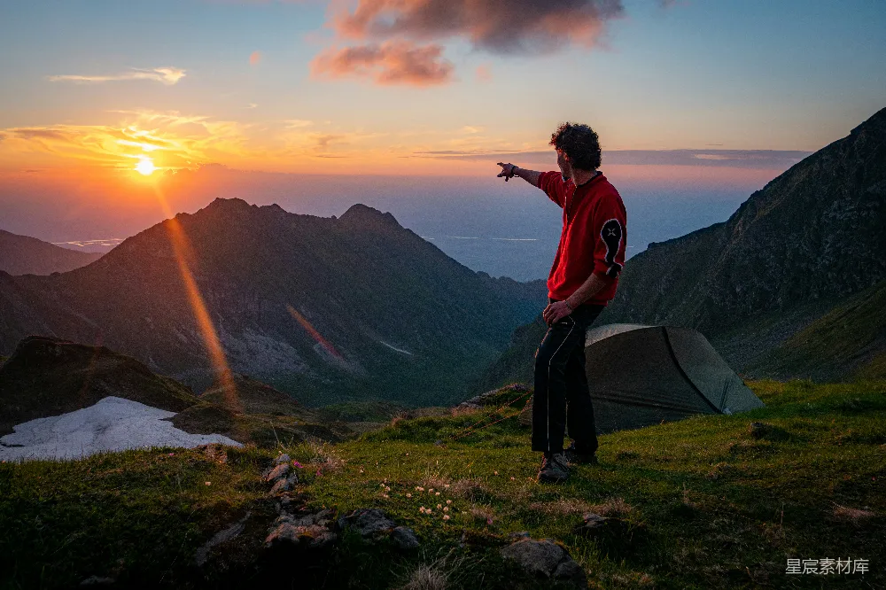 高清摄影  男人指着山顶风景中的落日，帐篷就在旁边。
