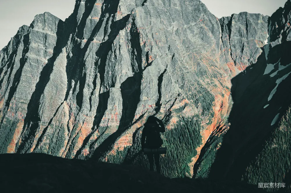 高清摄影  一个人站在绿色的草地上，背景是棕色的岩石山，时间是在白天。