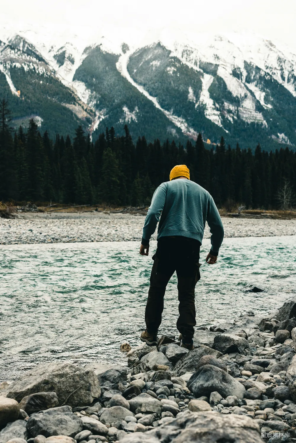高清摄影  一个男人正在一条岩石河床上行走，背景中有一座山。
