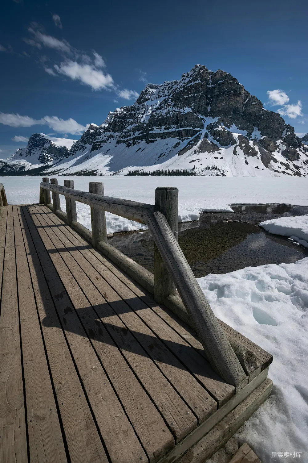 高清摄影  一座木桥横跨水面，背景是被雪覆盖的山脉。