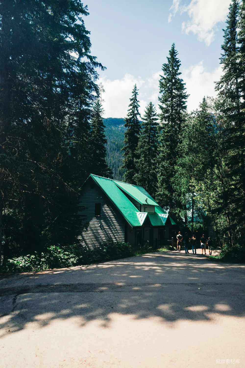 高清摄影  一个绿顶小屋隐藏在高大的树木和群山之间。