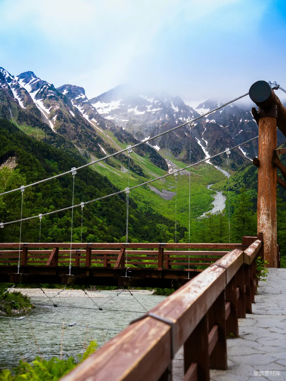 高清摄影  一座横跨河流的木制悬索桥，背景是雪山。