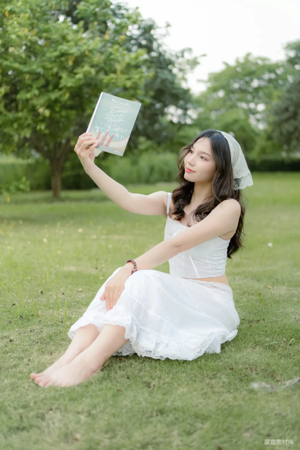 高清摄影  一个女人坐在草地上，手里拿着一本书。