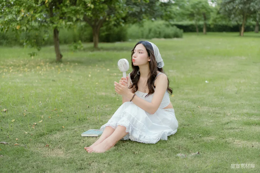 高清摄影  穿着白色连衣裙的女人坐在草地上。