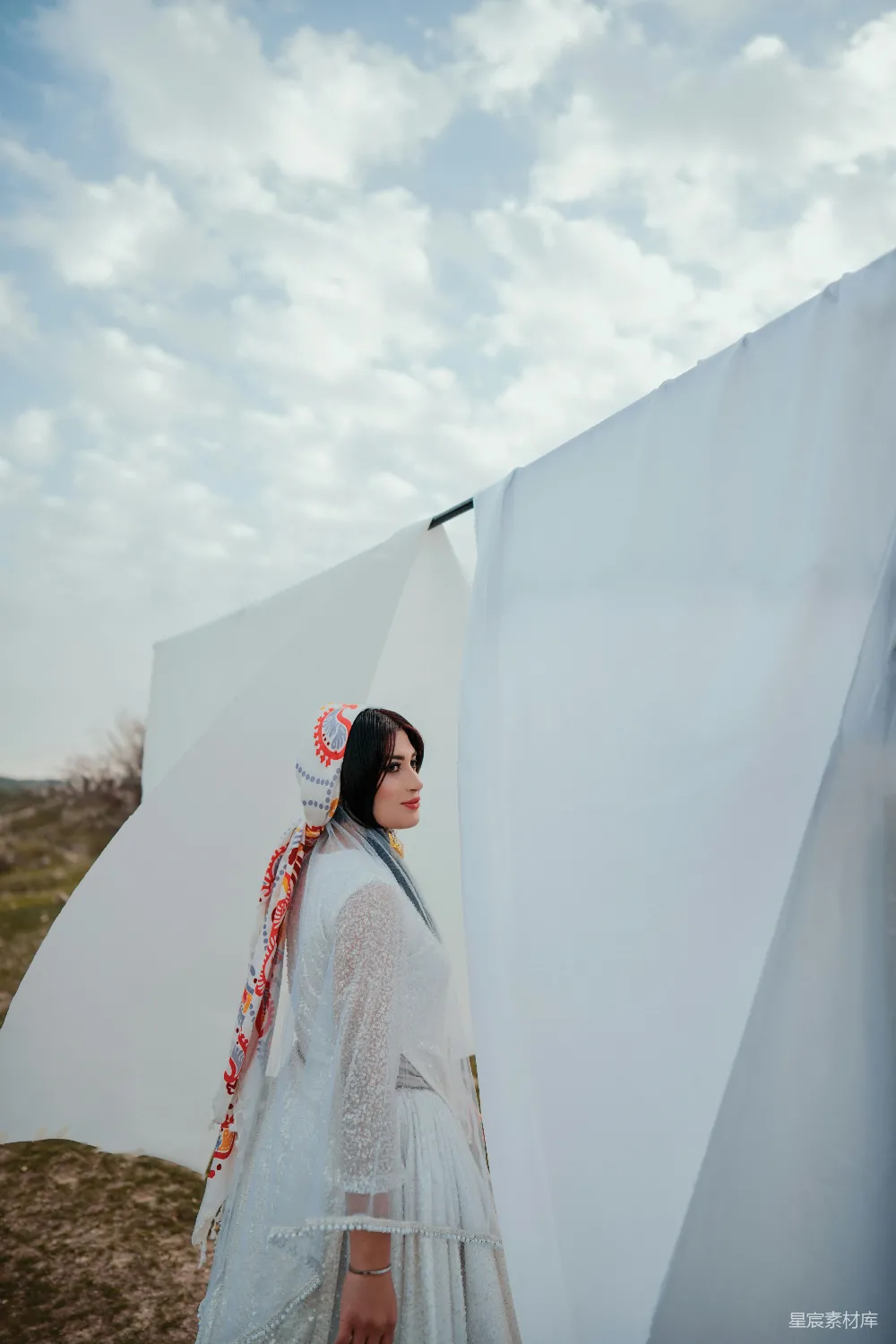 高清摄影  一个穿着白色连衣裙的女人站在一张白色的床单旁边。