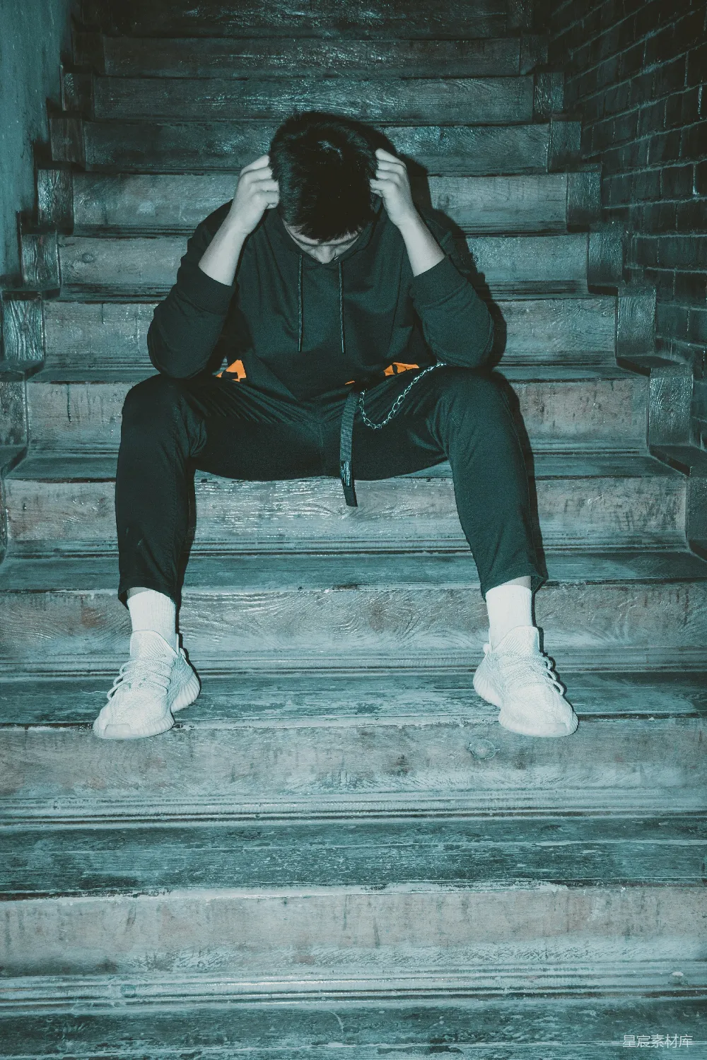 高清摄影  穿黑色连帽衫和黑色裤子的男人坐在楼梯上。