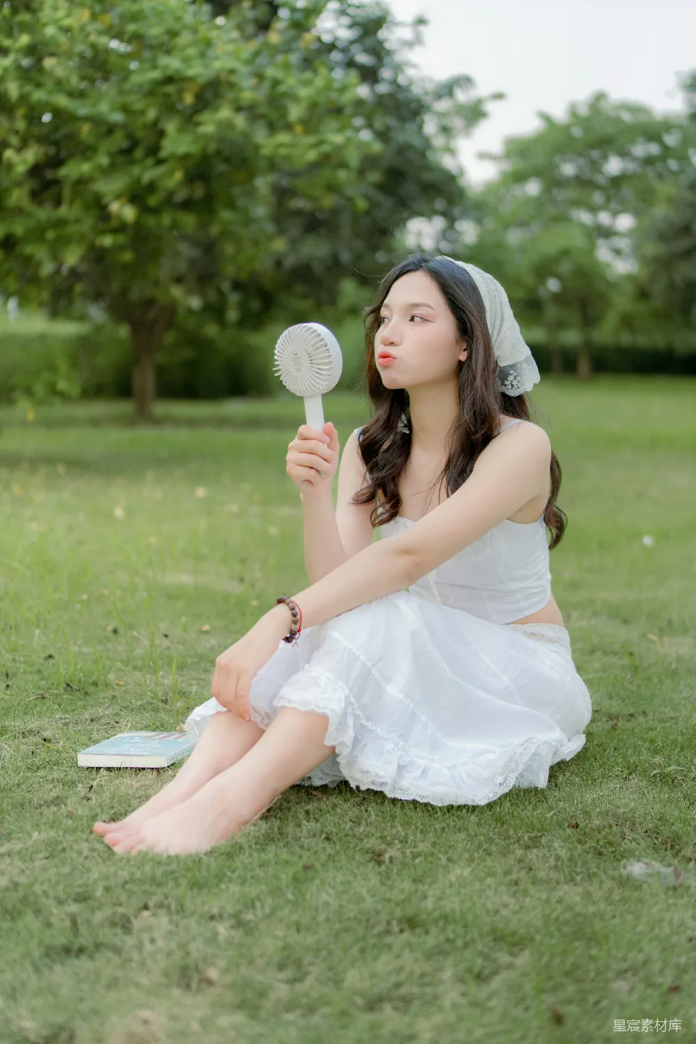 高清摄影  一位穿着白色连衣裙的女子坐在草地上。