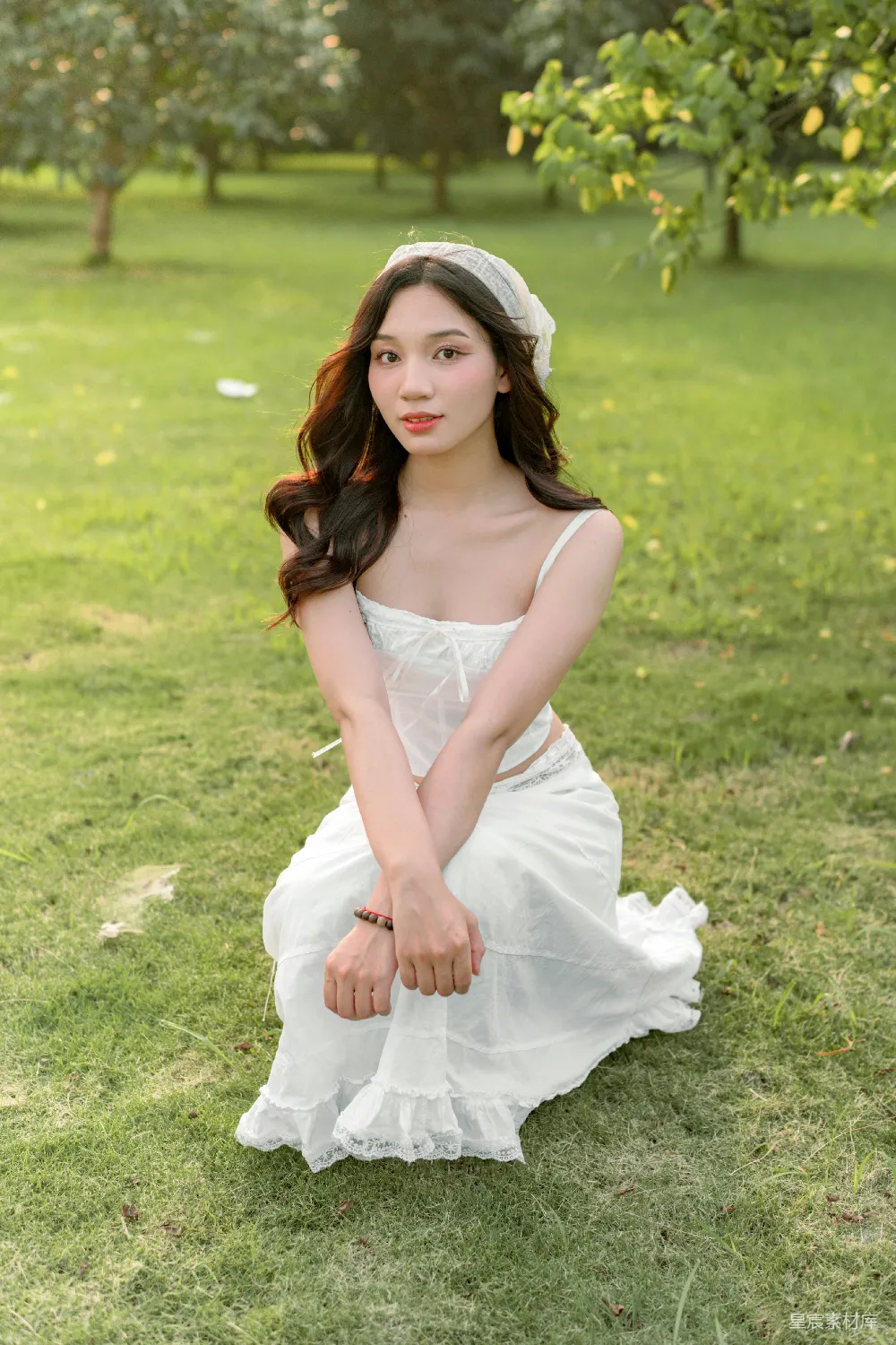 高清摄影  一位穿着白色连衣裙的女人坐在草地上。