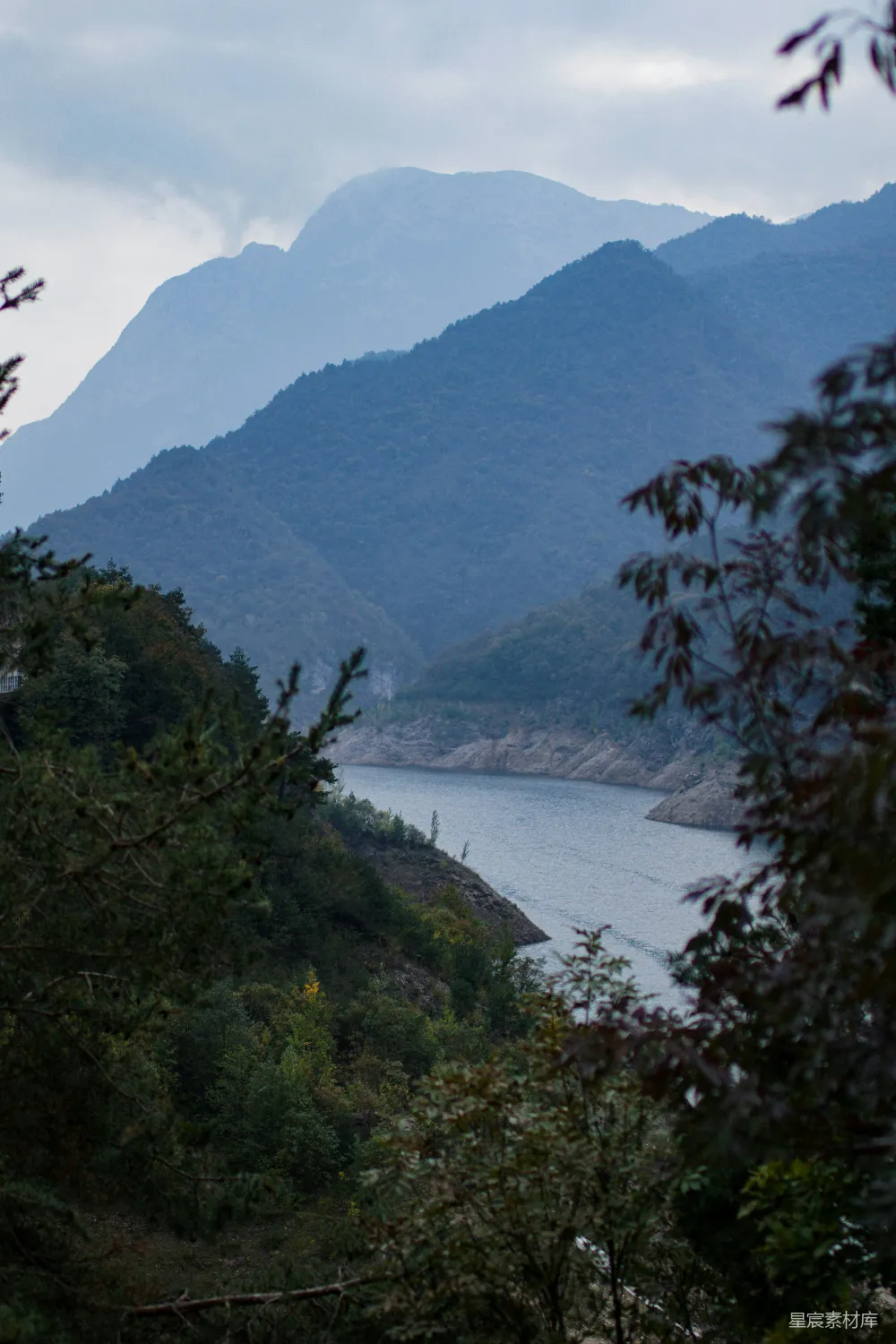 高清摄影  一片被树木环绕、远处有山的水域。