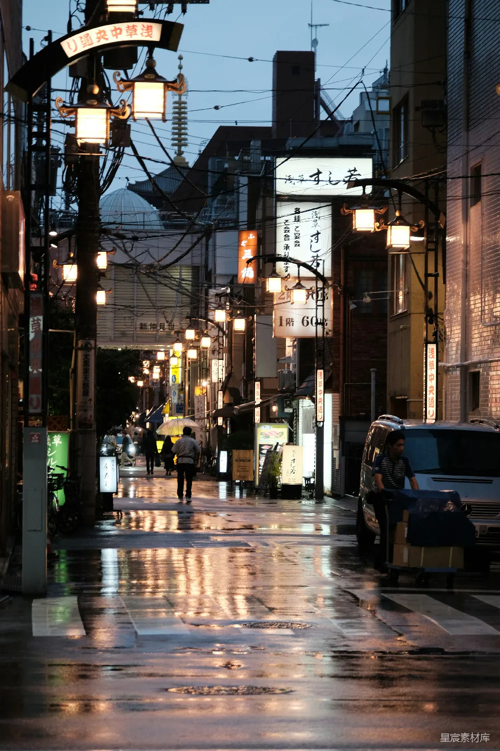 高清摄影  一条湿漉漉的夜晚城市街道，人们在人行道上行走。