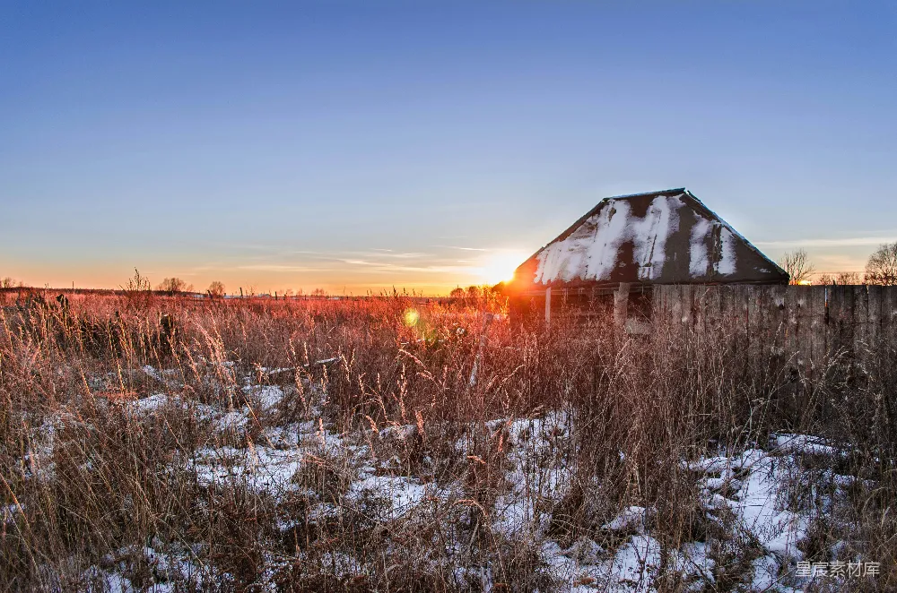 高清摄影  夕阳照耀在积雪覆盖的田野上，旁边有一座谷仓。