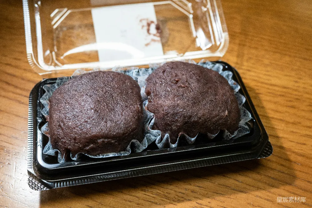 高清摄影  两个巧克力松饼放在塑料容器中，放在木桌上。