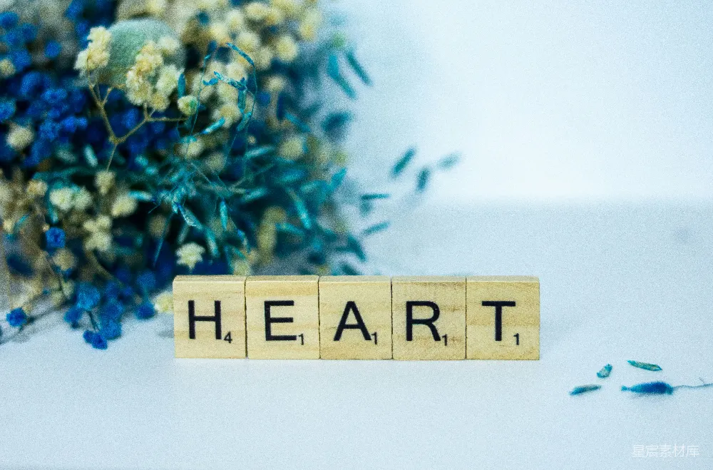 高清摄影  一个木制的方块，上面拼写着单词“heart”，旁边是一束花。