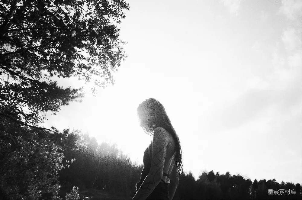 高清摄影  一个女人站在田野里，背景中有树木。