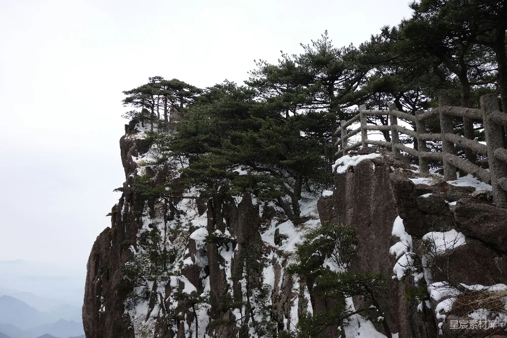 高清摄影  积雪覆盖的山崖，有树木和木制栏杆。
