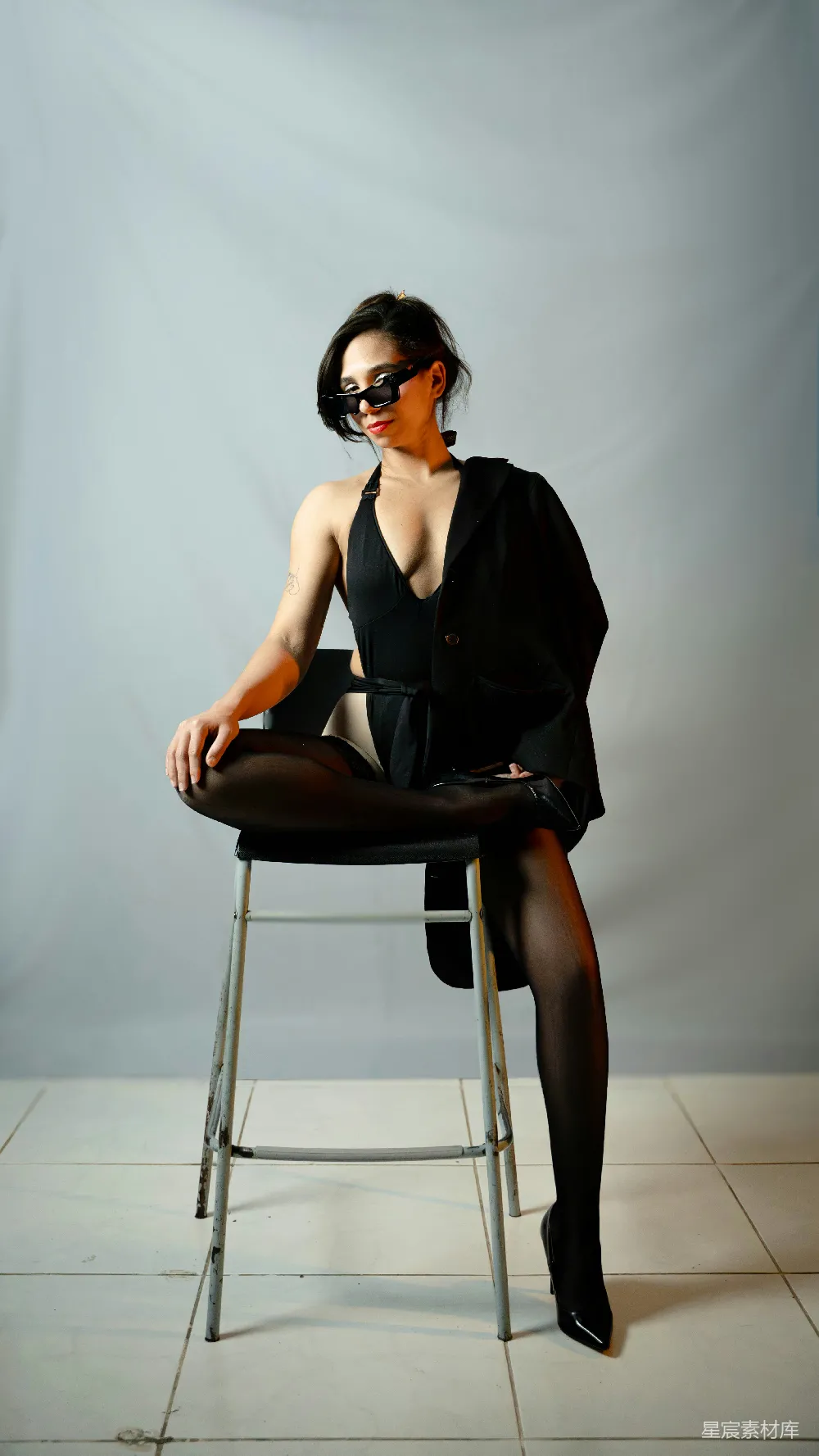 高清摄影  穿黑色泳衣和西装外套的女人坐在凳子上。