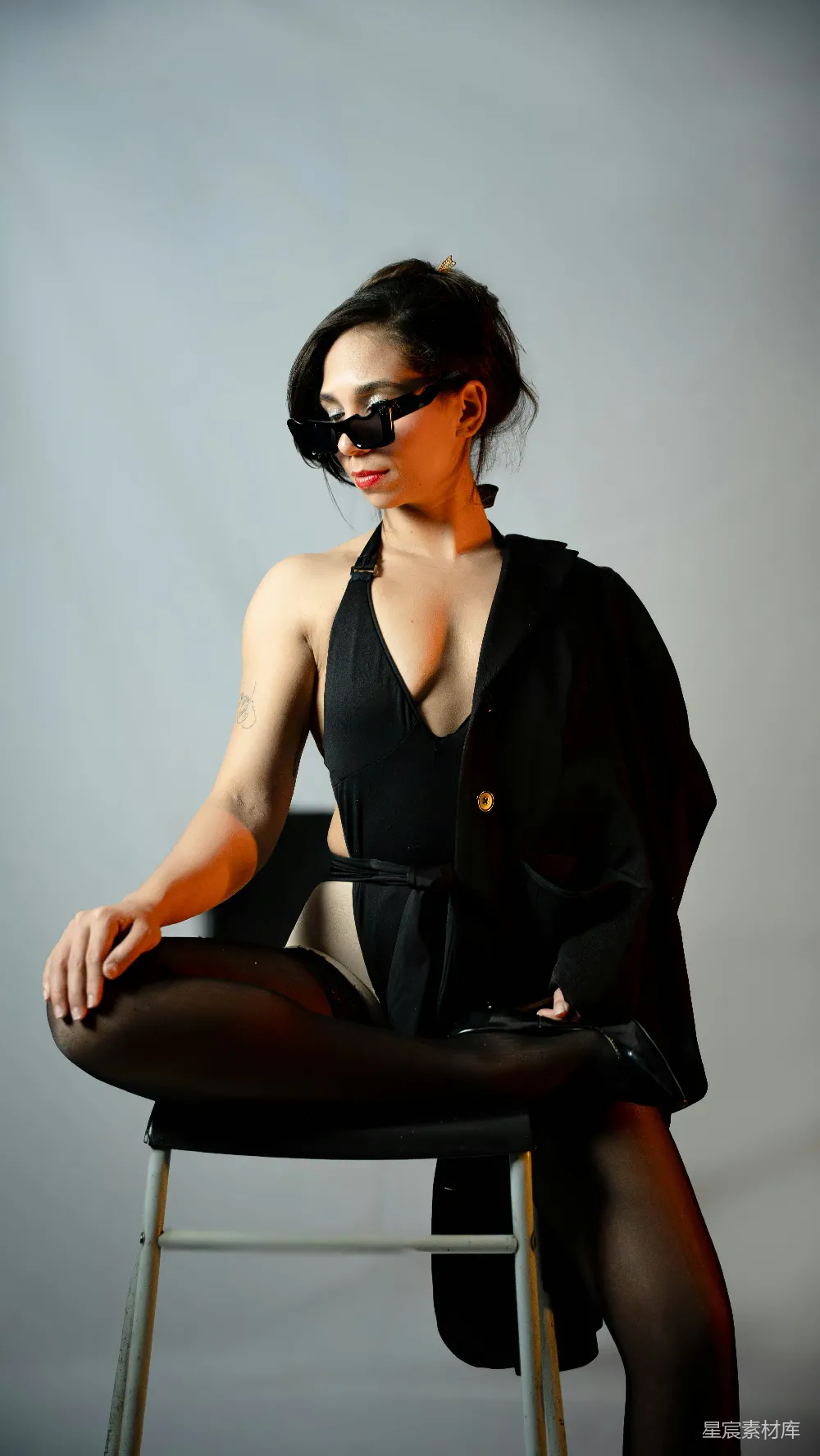 高清摄影  穿着黑色泳衣和西装外套的女人坐在椅子上摆姿势。