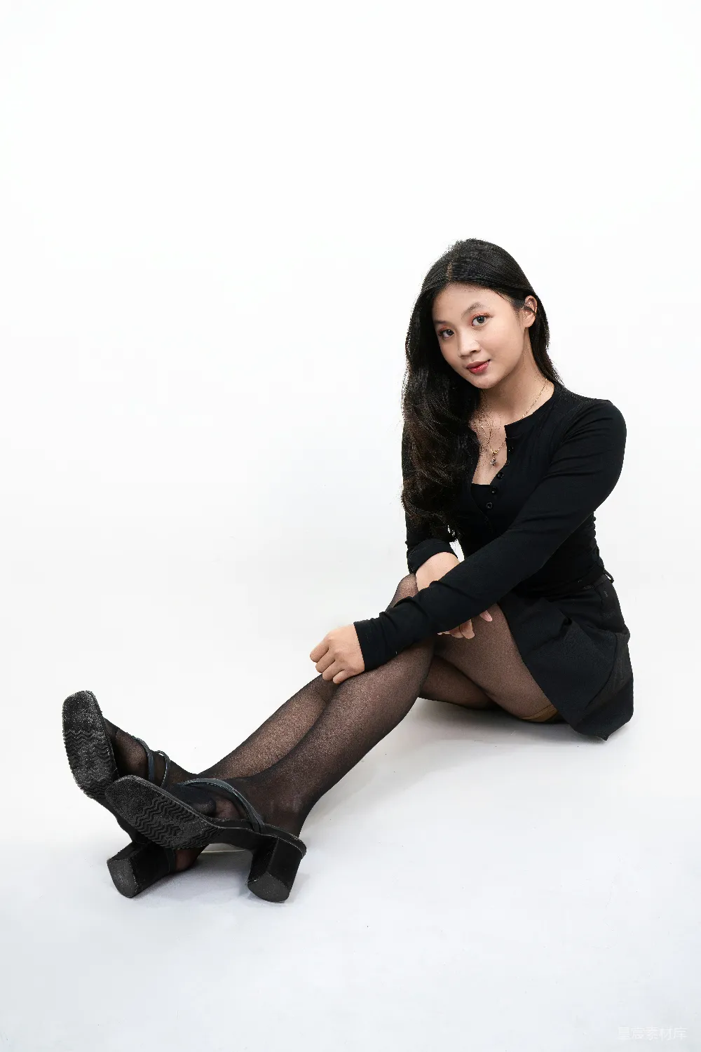 高清摄影  穿着黑色服装的年轻女子坐在白色背景前。
