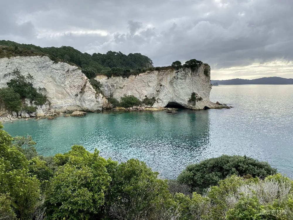 高清摄影  白天，蓝天白云下，蓝海上有岩石山旁的绿树。