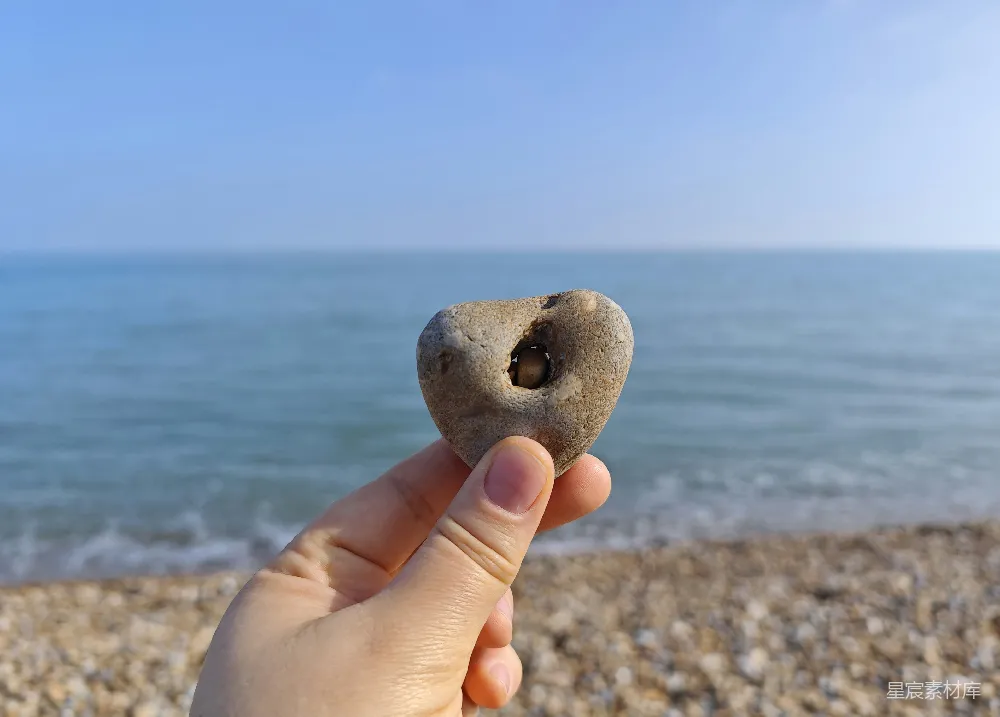 高清摄影  拿着一颗心形的石头，海景在后面。