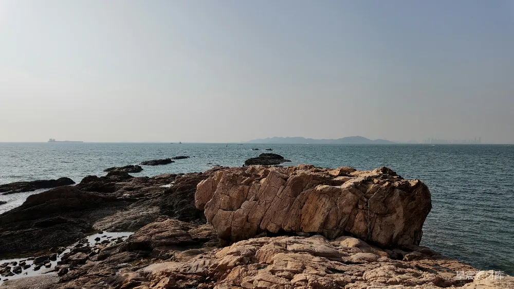高清摄影  岩石海岸线，平静的海面在薄雾笼罩的天空下。