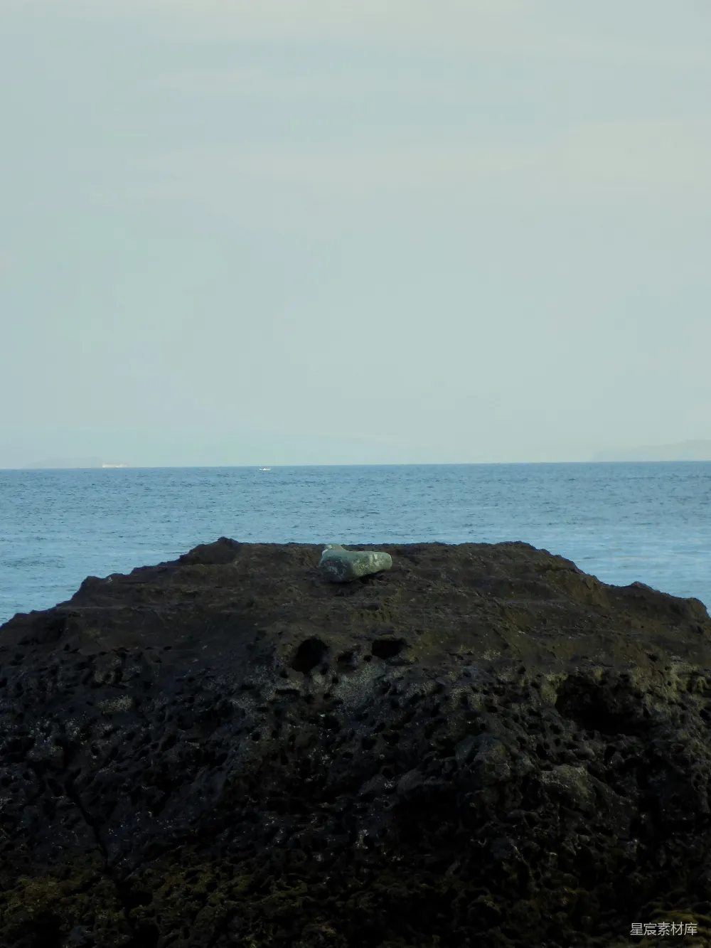 高清摄影  一块石头安静地坐落在海洋旁的深色岩石上。