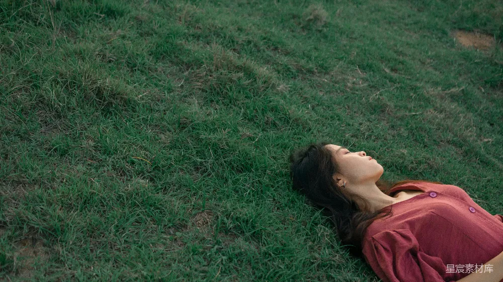 高清摄影  一个女人躺在草地上，闭着眼睛。