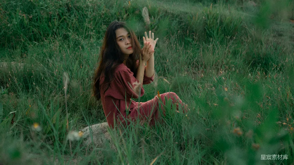 高清摄影  一个女人坐在田野里，双手举起来。