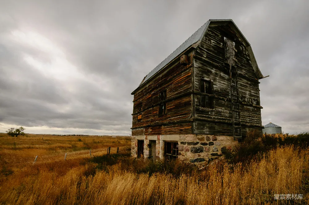 高清摄影  棕色的木屋坐落在棕色的草地上，天空灰蒙蒙的。