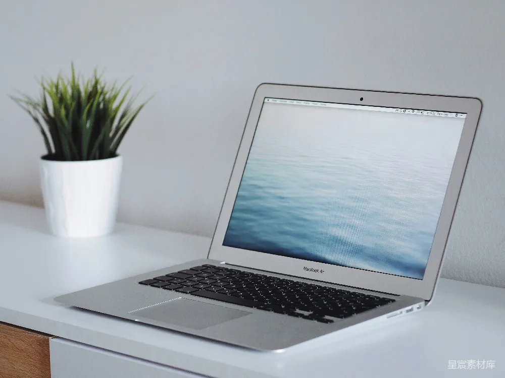 高清摄影  MacBook Air 靠在绿色植物旁，放置在白色木制表面上。