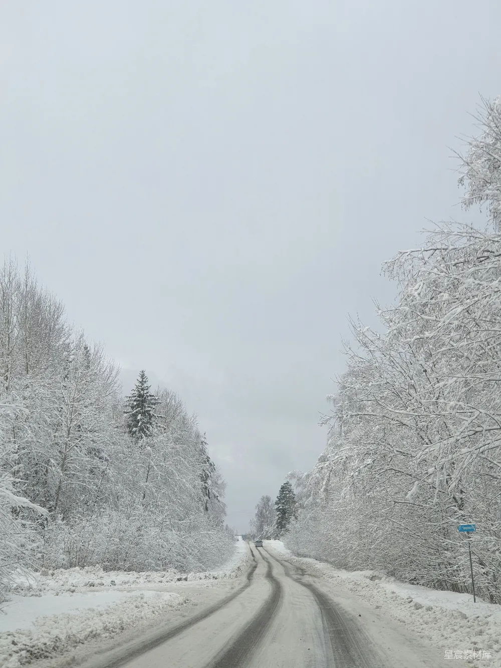 高清摄影 自然 一条被雪覆盖的道路，两旁有树木和一个蓝色的标志牌。