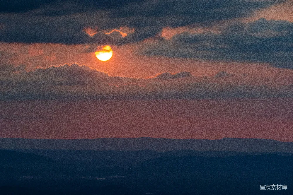 夕阳的余晖洒在山峦上，天空被染成橙红色，云层在夕阳的映照下呈现出柔和的轮廓，营造出一种宁静而美丽的自然景观。适合用于展示自然之美或表达内心的平静与宁静。