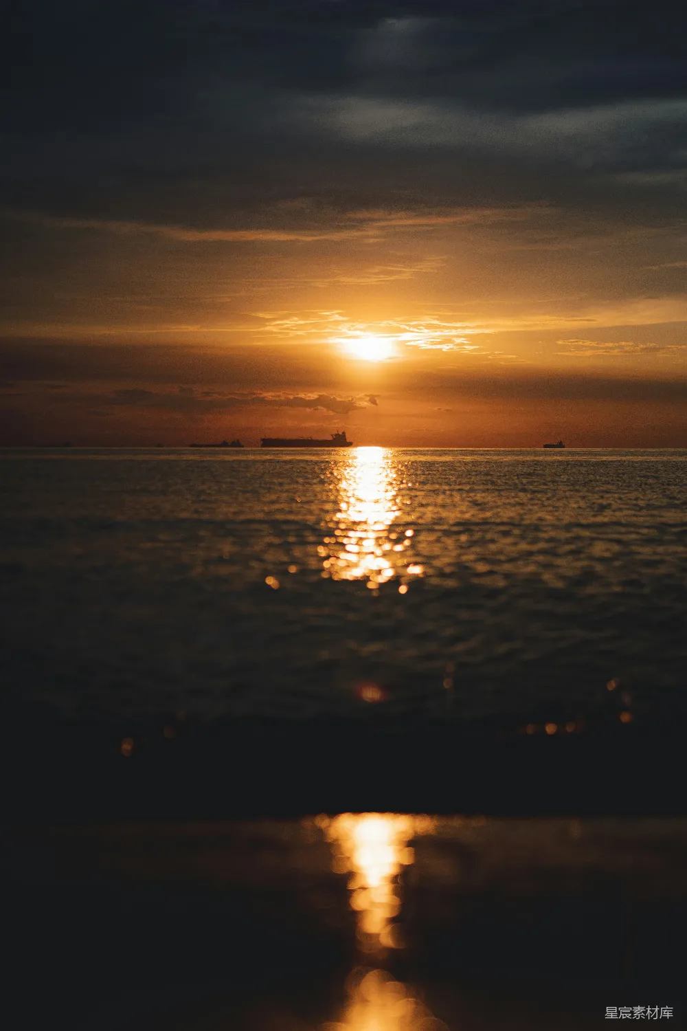 图片展示了一幅宁静的海面夕阳场景，夕阳的余晖洒在海面上，形成了耀眼的光斑。海平面上有几艘船只，天空中云层稀疏，整体氛围宁静而美丽。这种场景适合用于自然风光、旅行或海洋主题的背景图片。
