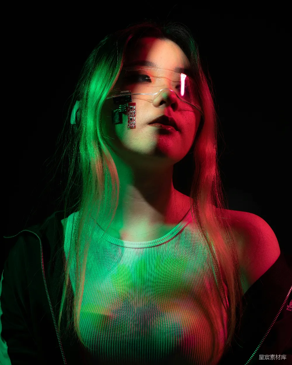 这张图片展示了一位女性，她戴着带有电路板的透明眼镜，背景是对比鲜明的红绿光影。她穿着紧身衣物，整体色调和光影效果营造出一种未来科技的氛围。这张照片适合用于科技、时尚或未来主义主题的广告或海报设计。