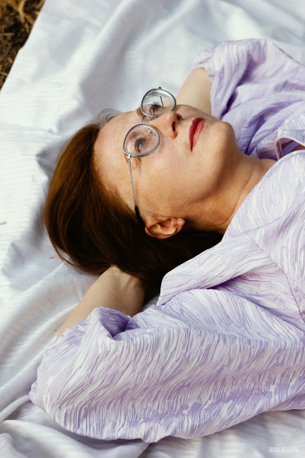 高清摄影 女性 休闲 自然 放松 户外 悠闲时光：戴眼镜的女性躺在白色毯子上