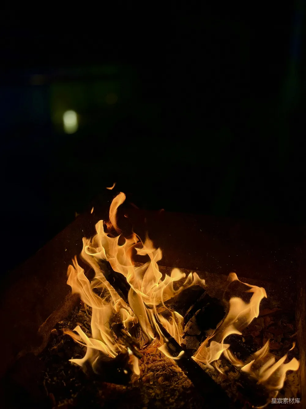 这张图片展示了夜晚篝火的景象，火焰在黑暗中燃烧，温暖的光芒照亮了周围的环境。火光摇曳，营造出一种宁静而温馨的氛围，适合用于表达自然之美、夜晚的宁静或户外活动的场景。