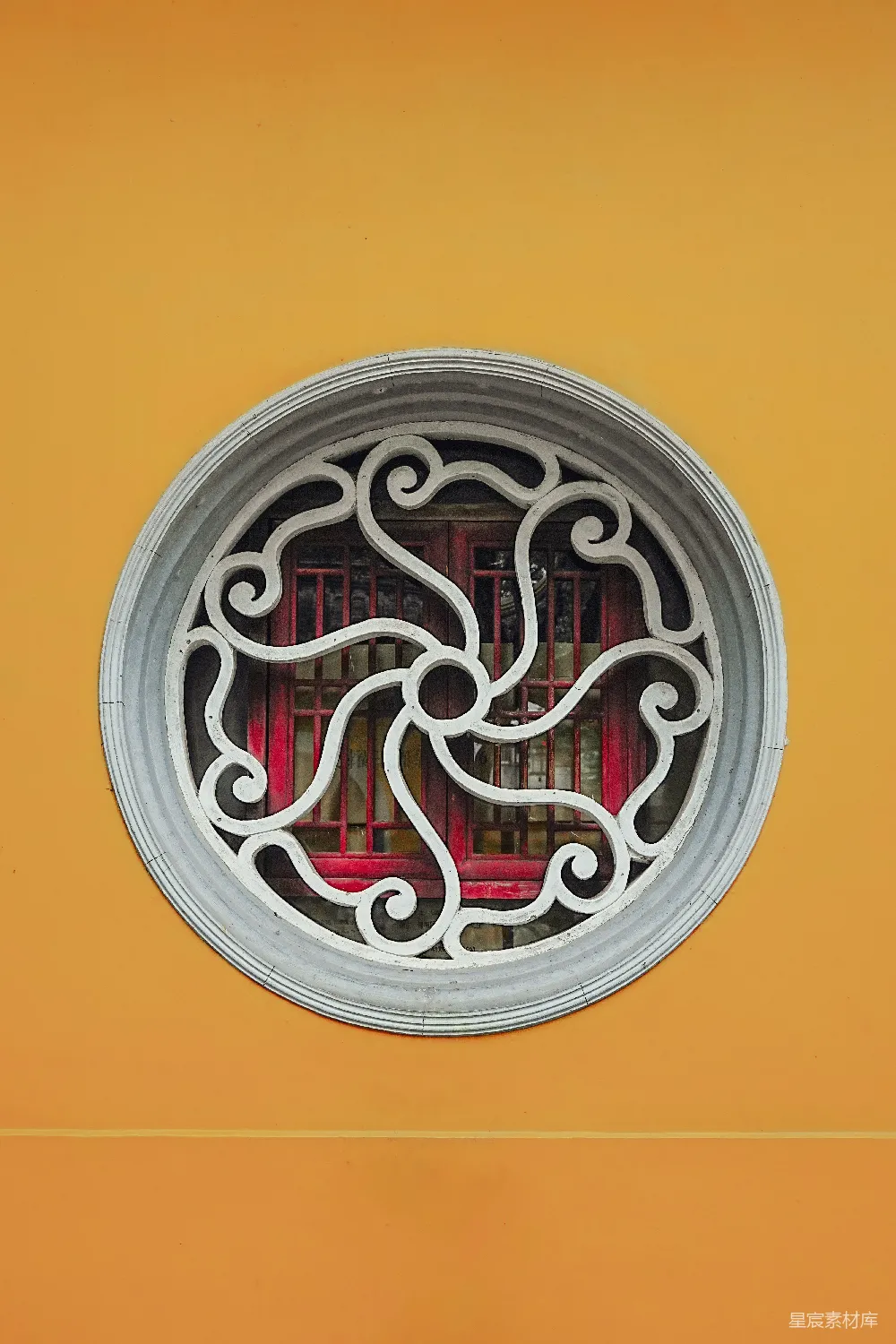 这张图片展示了一扇传统中式建筑的窗花，窗框为白色，窗棂设计复杂，图案呈现出对称的花纹，背景是温暖的黄色墙面。这种窗花不仅具有实用性，还体现了中国传统文化中的美学理念，适合用于建筑装饰或文化展示。
