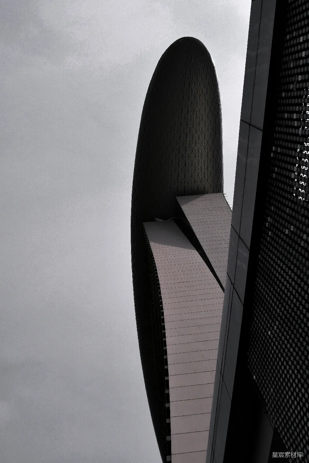这张图片展示了一座现代建筑的特写，其独特的几何形状和简洁的线条在灰色调的背景下显得尤为引人注目。建筑的外观设计融合了未来感和实用性，适用于展示现代城市建筑风格的素材。