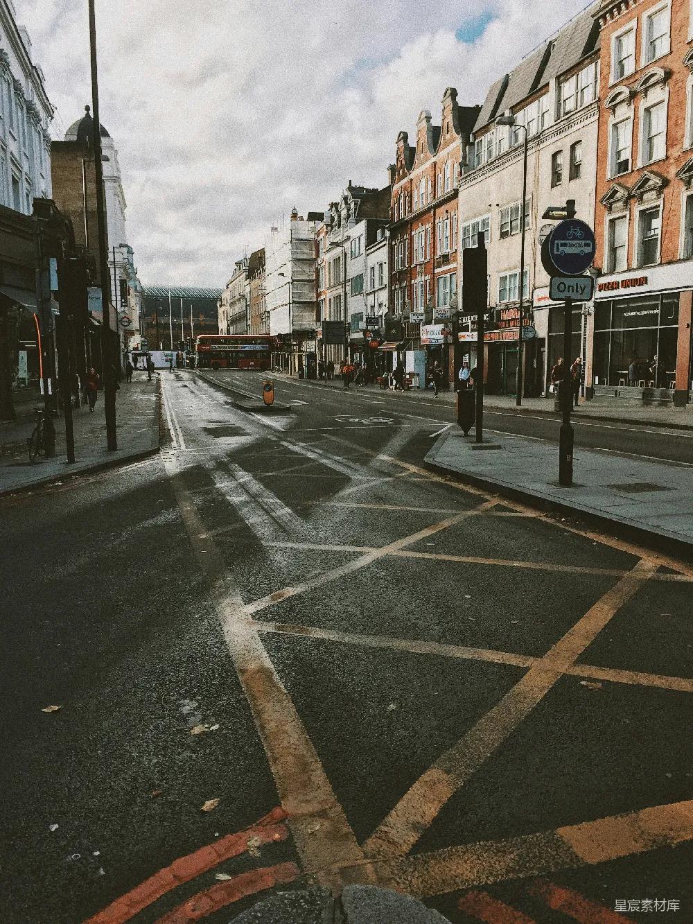 这张图片展示了一个伦敦街头的景象，道路上有清晰的交通标线，两旁是历史建筑，街道上行人稀少，天空中有一些云彩，给人一种宁静的感觉。