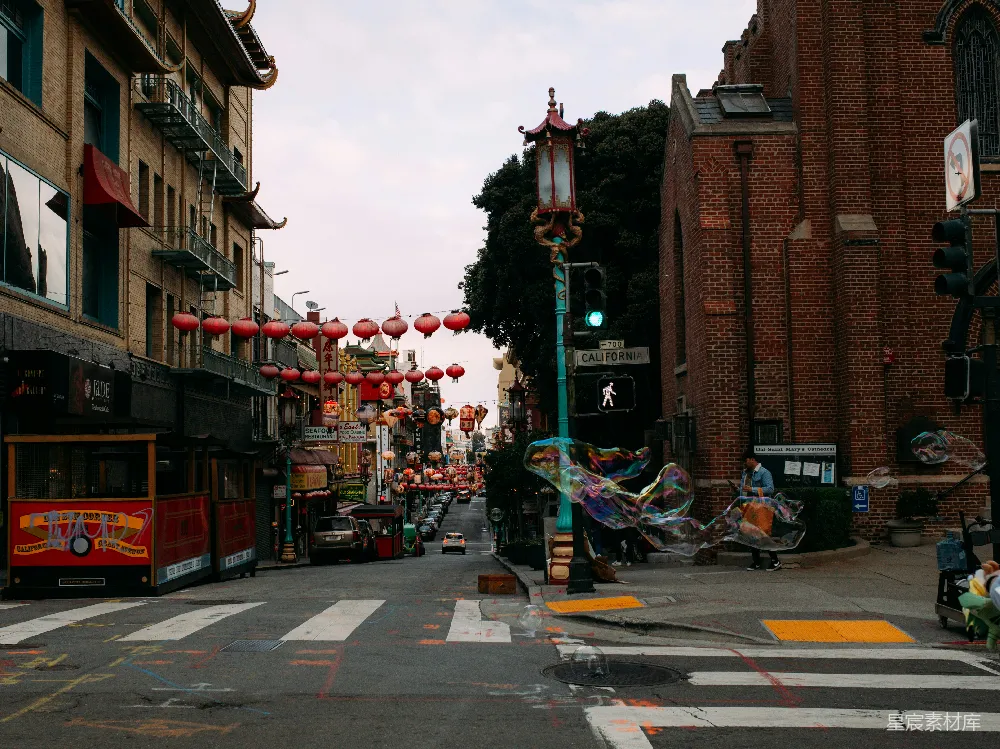 这张图片展示了旧金山唐人街的一个宁静角落。街道两旁是传统的中式建筑，挂着一串串红色的灯笼，营造出浓厚的节日氛围。街道的一侧有一个大型的彩色泡泡装置，增添了现代与传统交融的美感。远处的建筑物和路标显示了这是一个典型的美国城市街道，而近处的细节