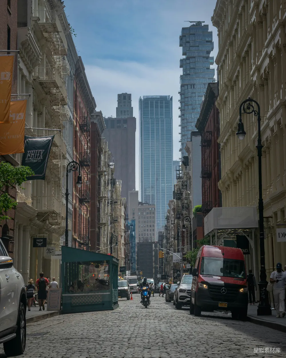 这张图片展示了纽约市的一条街道，两侧是传统的建筑和现代的高楼。街道上铺着石板，车流和行人穿梭其间，背景中高耸的摩天大楼与街道两侧的建筑形成鲜明对比。这幅画面捕捉了城市生活与建筑美学的双重魅力，适合用作城市风光或旅游宣传图片。