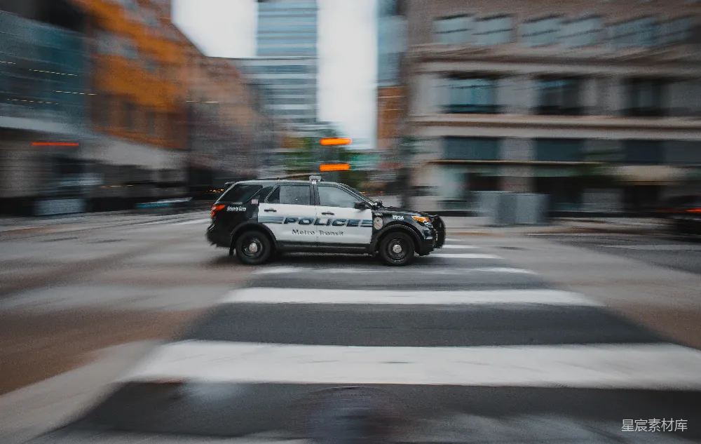 这张图片展示了一辆警车在城市街道上疾驰的场景，背景模糊，突出了车辆的动感和速度感。图像通过模糊效果传达了运动的瞬间，适合用作城市生活、交通安全或警力主题的背景素材。