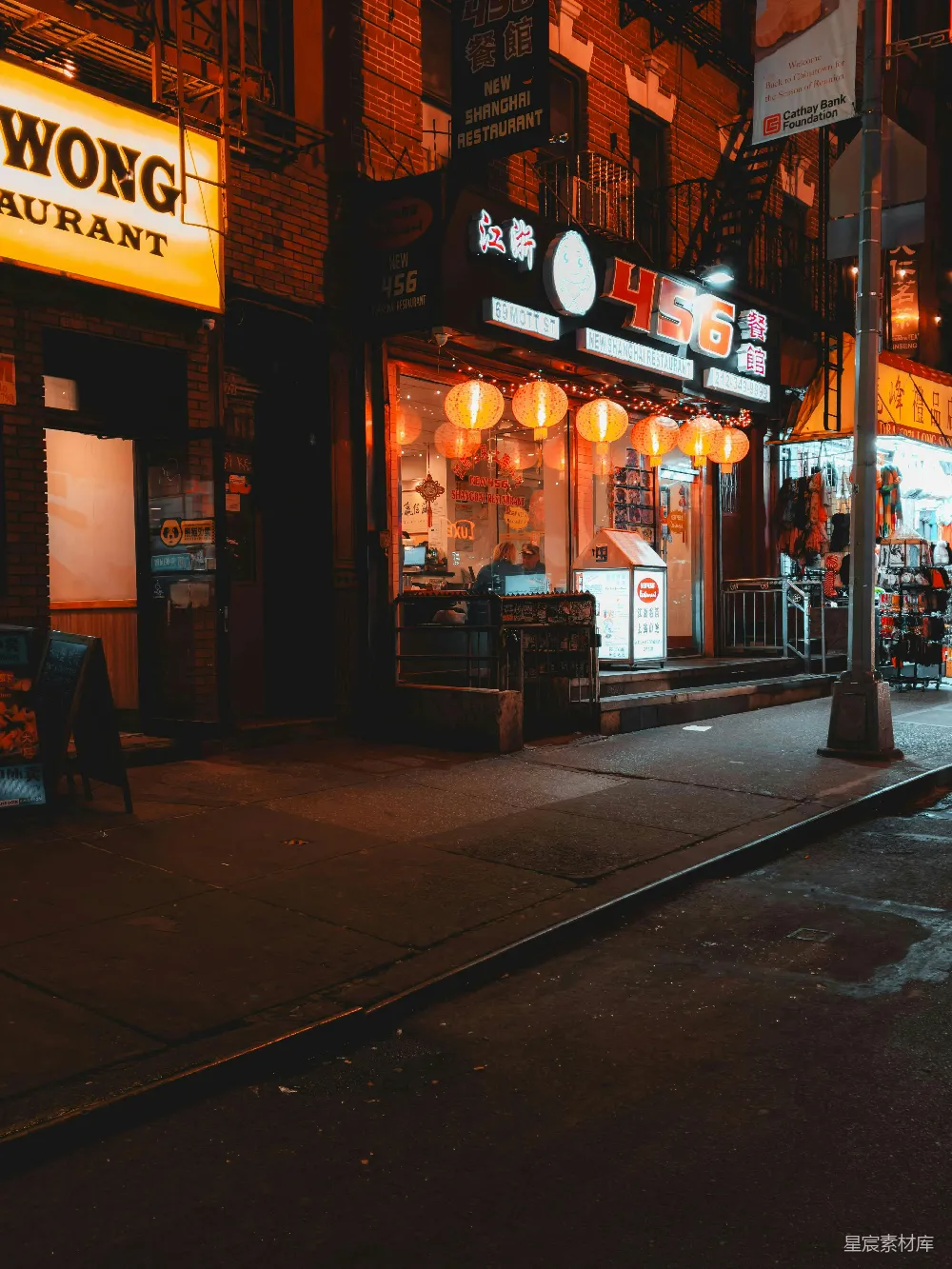 这张图片展示了纽约唐人街的夜景，灯光下的餐厅和商店显得格外温馨，红灯笼和招牌在夜色中显得格外醒目。街道两旁的建筑和商店营造出一种独特而热闹的氛围。适合用于城市夜景、美食文化或旅游宣传。