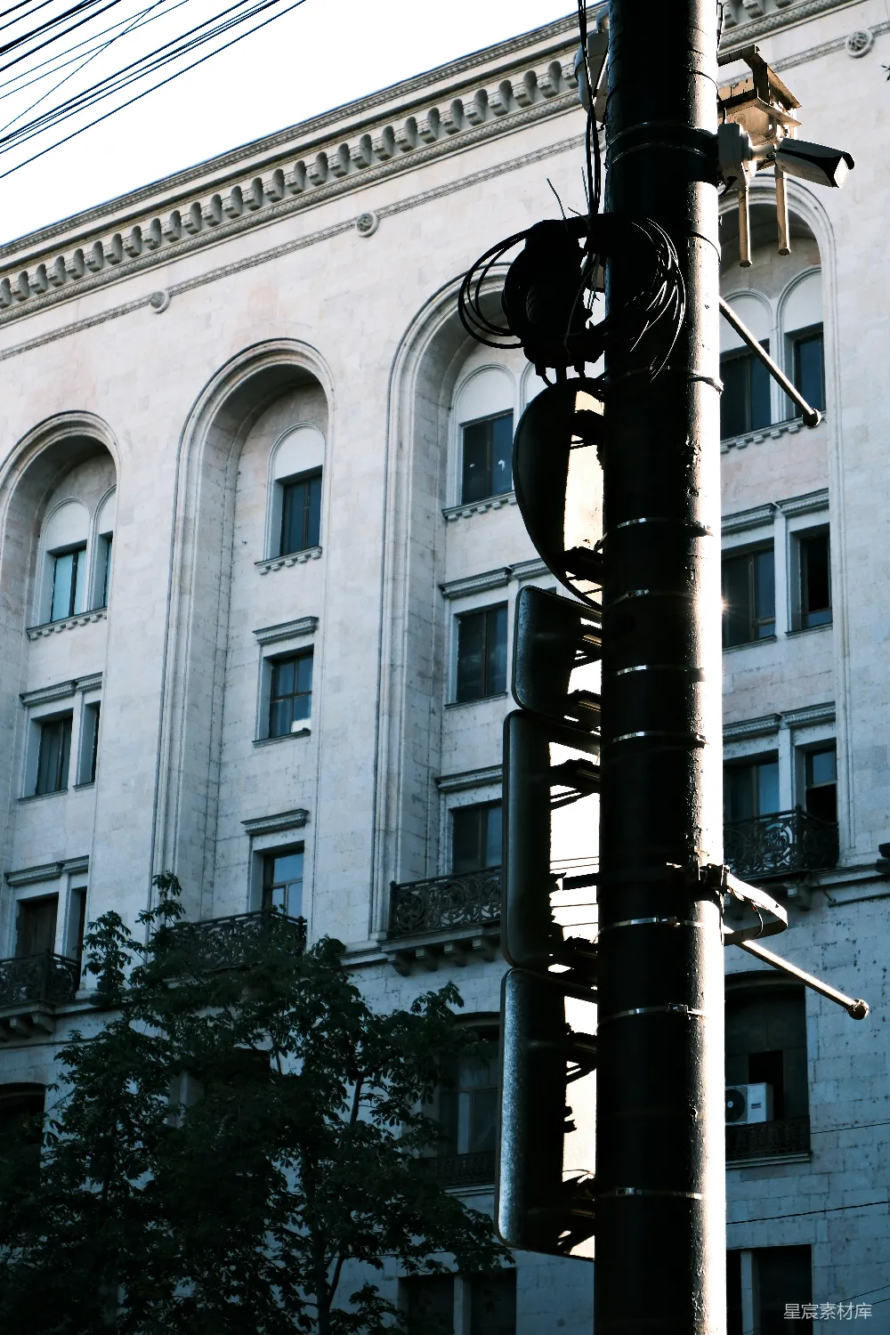 这张图片展示了一根电线杆，上面装有监控摄像头和各种电线，背景是一座古典风格的建筑。阳光从右侧照射过来，形成了柔和的光影效果。整体画面简洁而富有都市气息，适合用作城市生活或监控系统的主题图片。