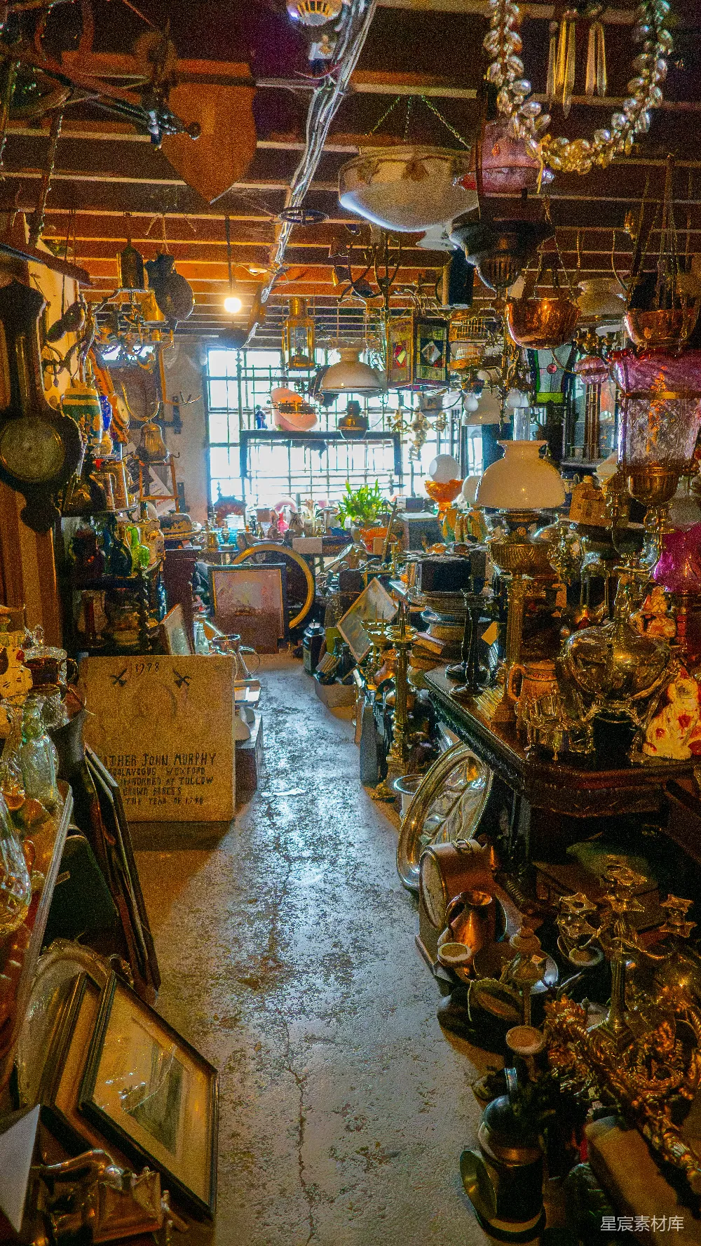图片展示了一个充满各种古董的室内场景，从天花板到地板，到处都是琳琅满目的老物件。阳光透过窗户洒进来，给整个空间增添了一丝温暖的氛围。这不仅是一个收藏品的展示，更像是一条时光隧道，让人仿佛能穿越到过去。