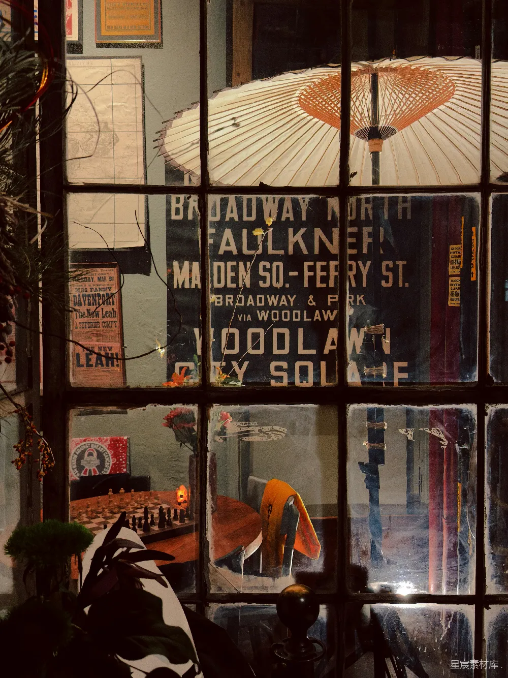 这张图片展示了一扇复古风格的窗户，透过窗户可以看到一个室内场景，窗上贴有“Broadway North”等字样。窗户内有棋盘、伞和一些装饰品，营造出一种怀旧的氛围。适合用于复古风格的室内装饰和怀旧主题的背景图片。