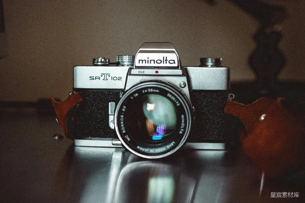 这张图片展示了一台Minolta SR T 102相机，镜头清晰可见，背景模糊，突出了相机的细节和质感。适合用于复古摄影爱好者、胶片摄影和摄影器材展示等场景。