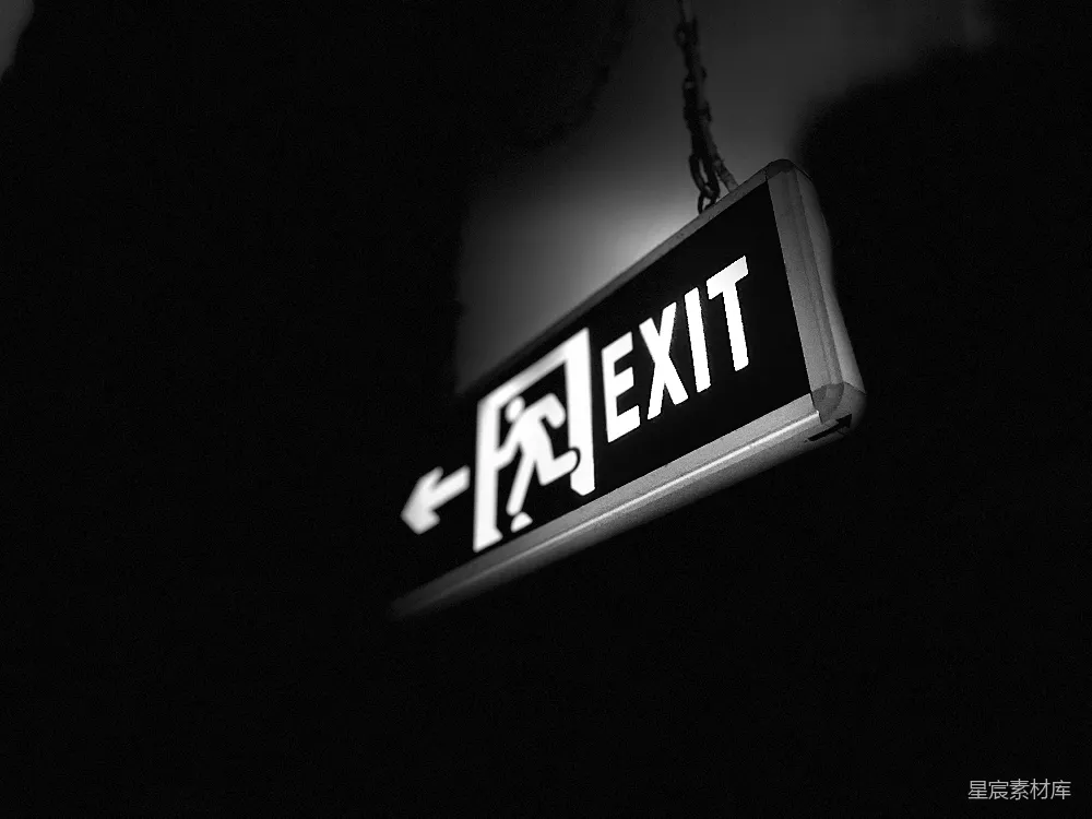 这张图片展示了一个黑色背景下的白色出口标志，标志上有一个向左的箭头和“EXIT”字样，背景是深色的，营造出一种神秘和紧急的氛围。这种场景通常用于建筑物的安全指示，提醒人们在紧急情况下找到出口。