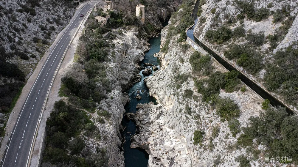 这张图片展示了一条蜿蜒的公路穿过峡谷，两旁是陡峭的岩石和郁郁葱葱的植被。一条清澈的河流从峡谷中流过，与公路平行。整个场景充满了自然的壮丽与宁静。适合用于展示自然景观、旅行、冒险主题。